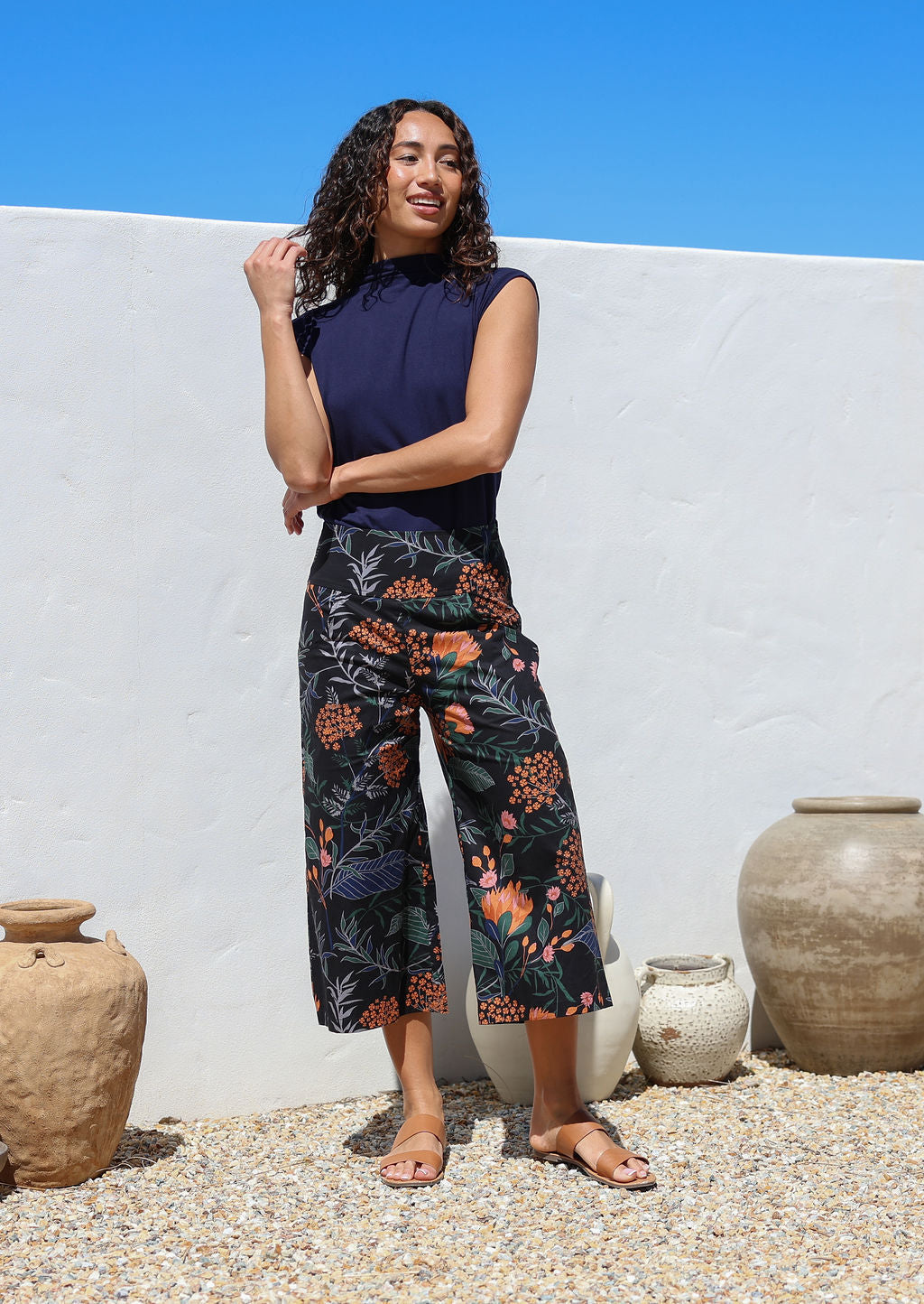 Woman wearing a navy blue top with high waisted, wide leg, capri style cotton pants, standing in front of the white wall