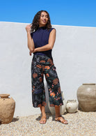 Woman wearing a navy blue top with high waisted, wide leg, capri style cotton pants, standing in front of the white wall