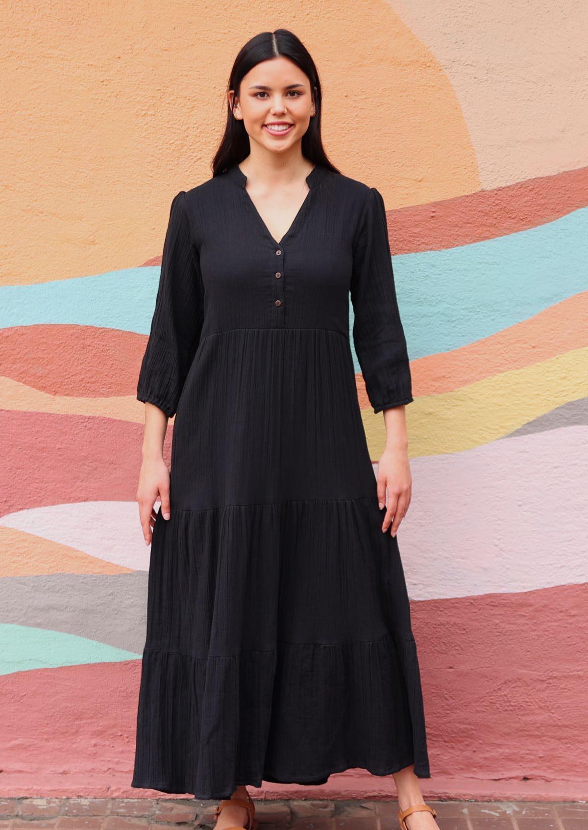 woman wearing long sleeve black cotton maxi dress in front of sun mural 
