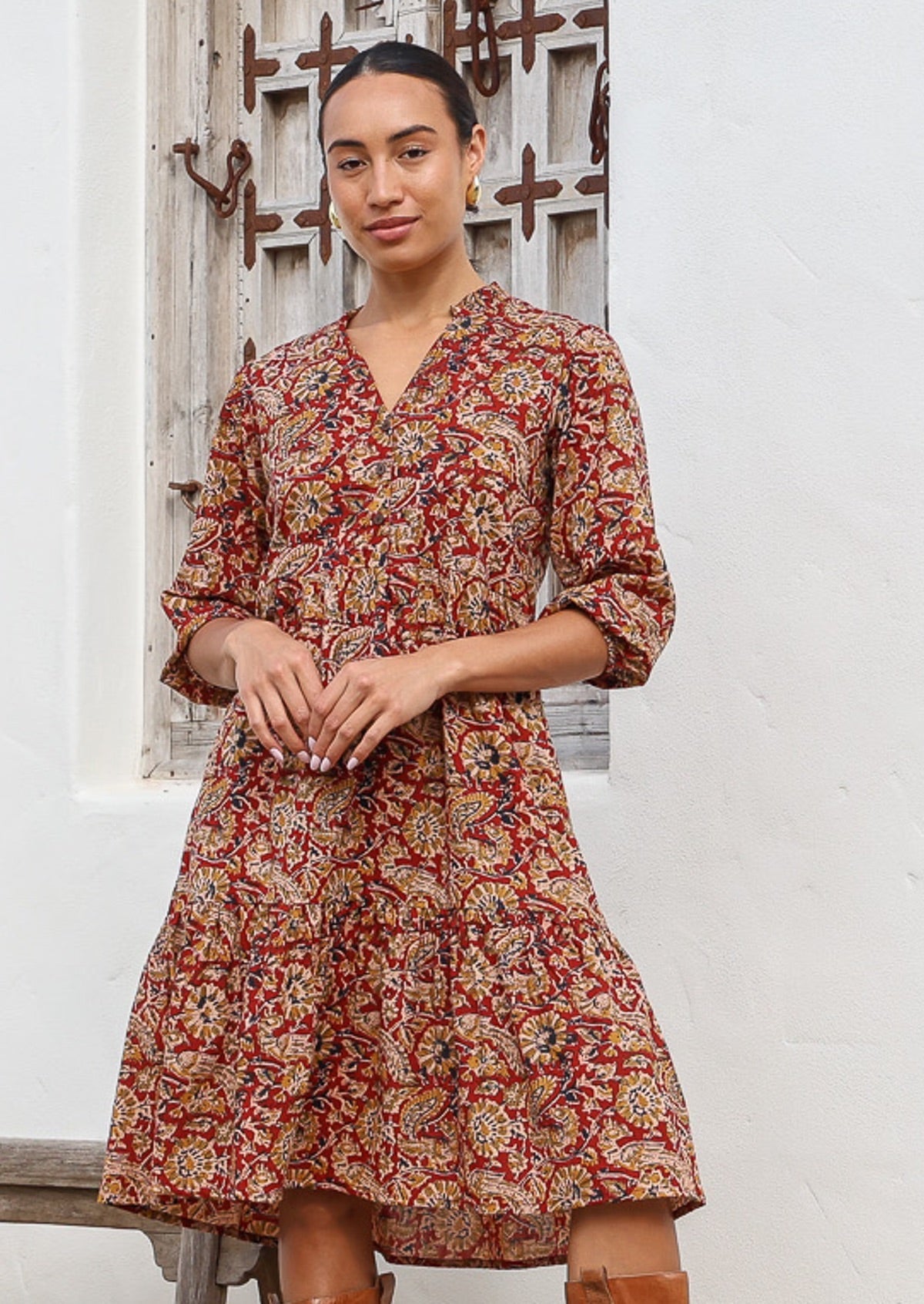 Woman poses in cotton tiered over the knee dress with 3/4 sleeves, buttoned bodice and V-neckline