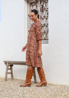 Model stands side on in cotton over the knee length relaxed fit dress with 3/4 sleeves, paired with tan boots 