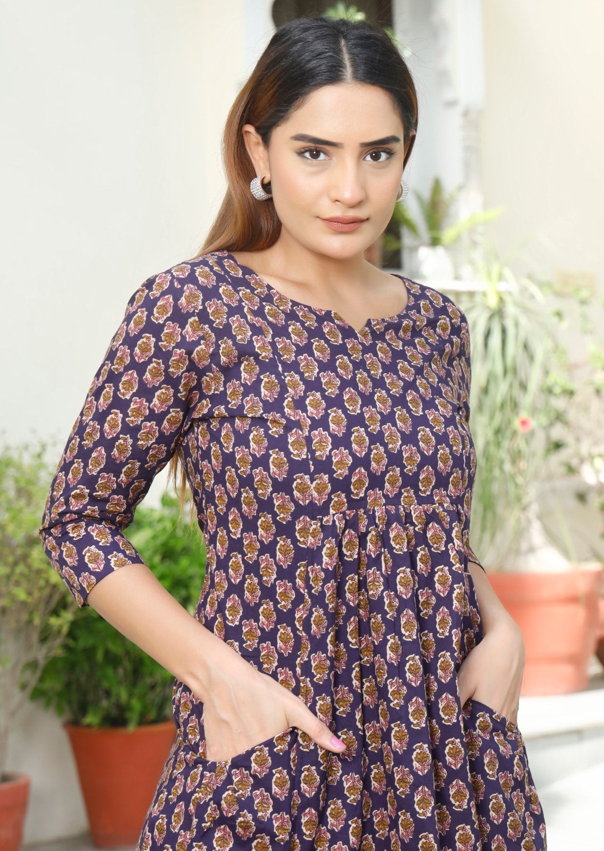 Close up image of model wearing purple floral printed, relaxed fit dress with small pin tucks below the bust. 