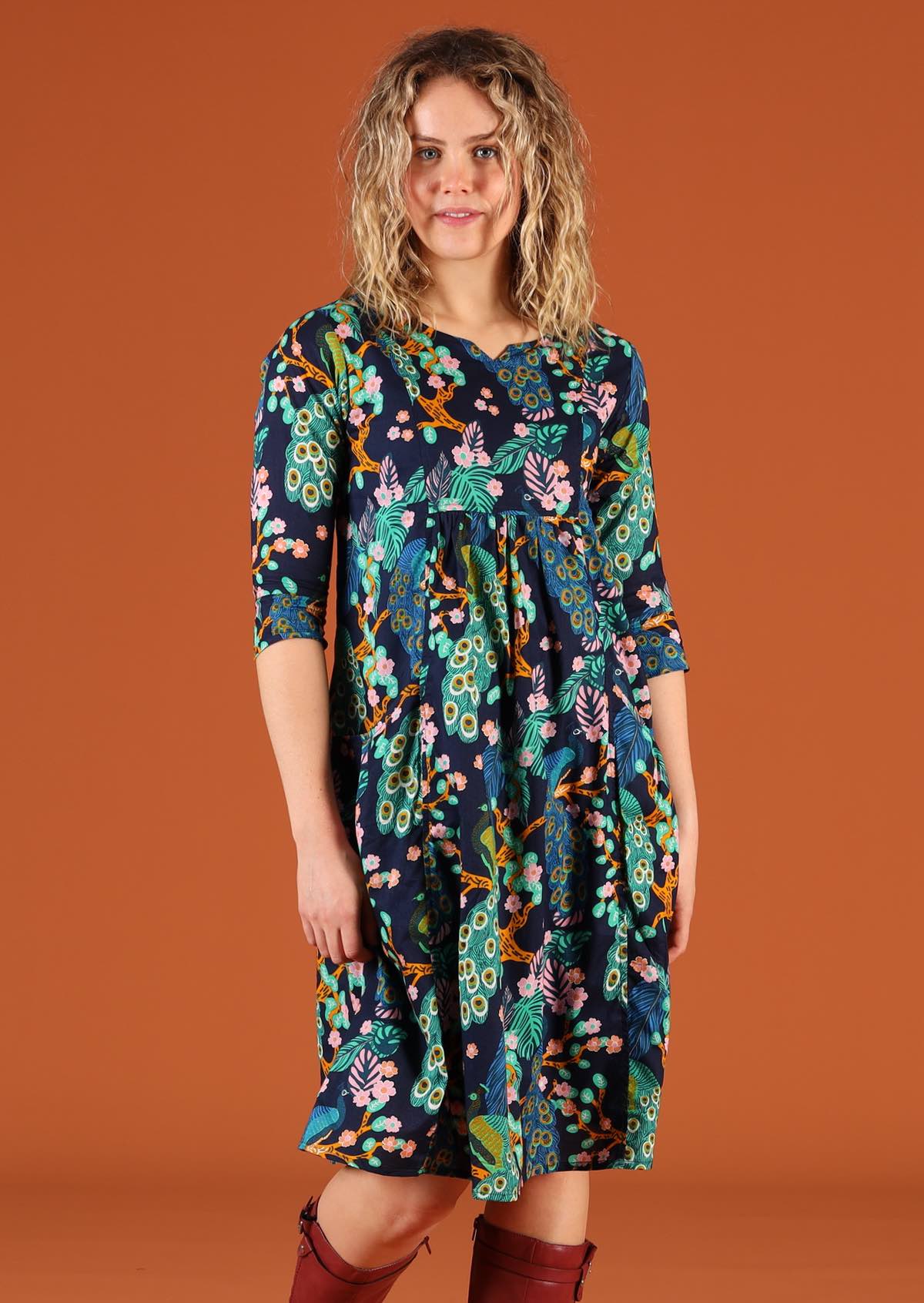 Model wearing a peacock print cotton dress with 3/4 sleeves and a small V in the round neckline