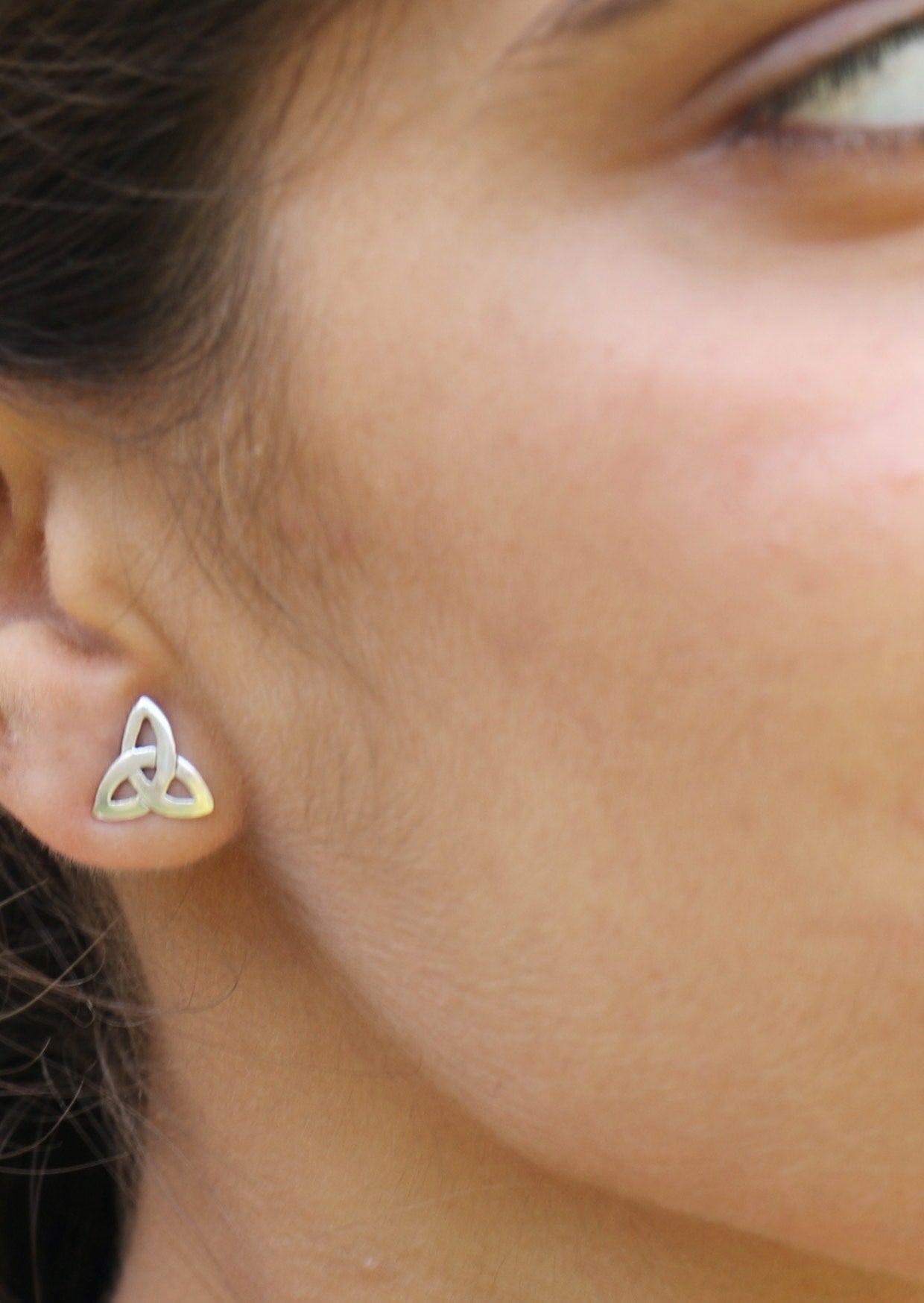 Close-up of an ear wearing a silver Trinity knot studs