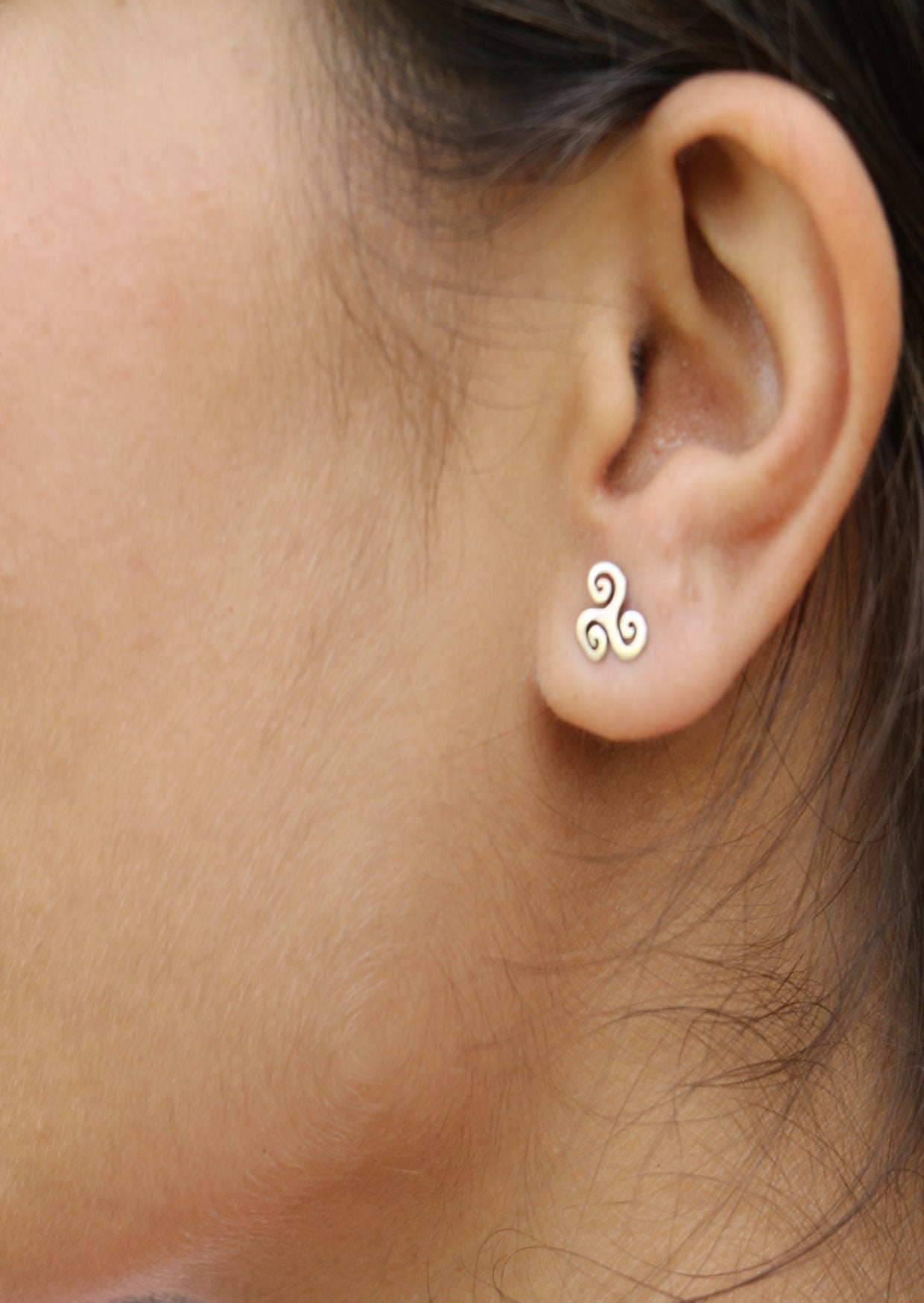 Close-up of an ear wearing a sterling silver Triskele studs with three swirling spirals radiating from center