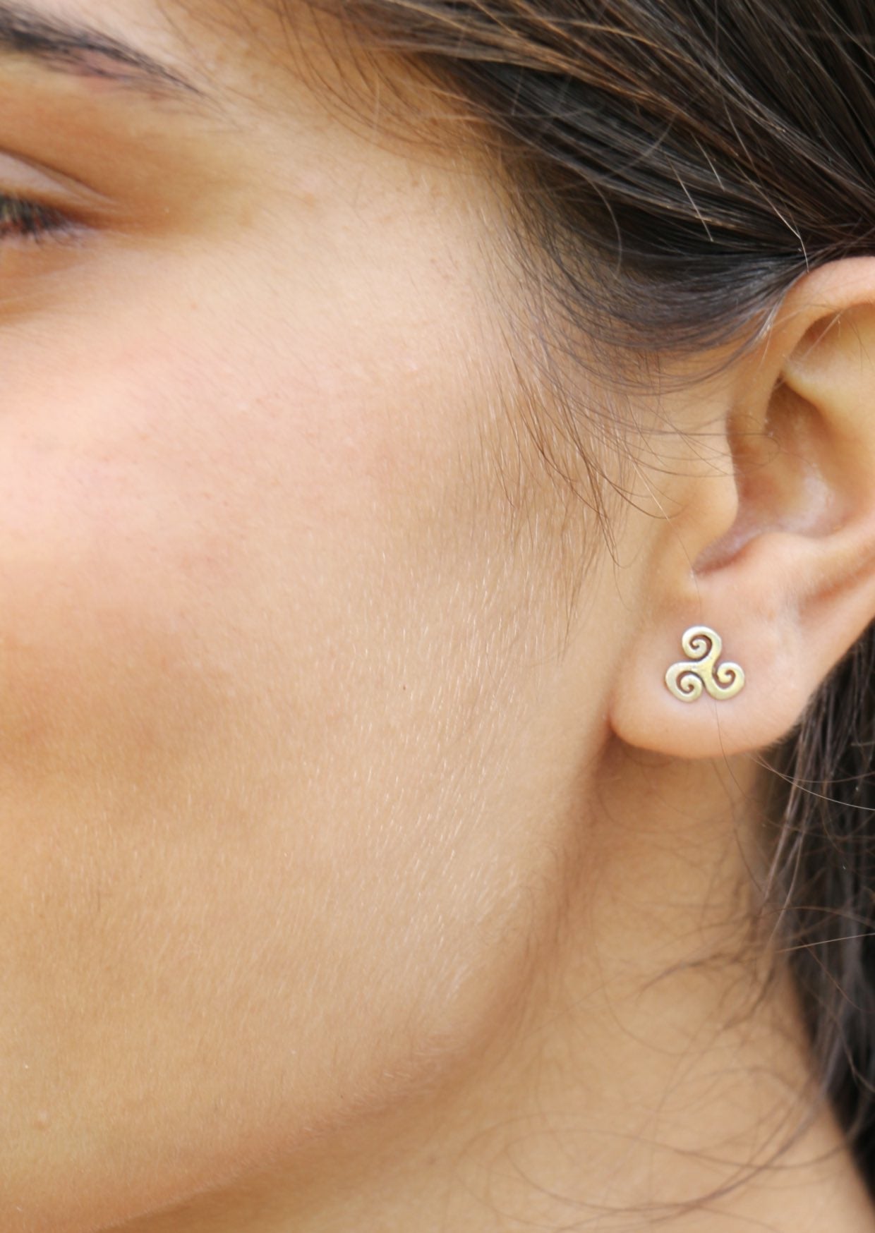 Close up of a woman wearing small triskele silver studs with butterfly backs 