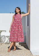 Woman wearing a pink floral cotton midi dress standing against a white wall with blue sky.