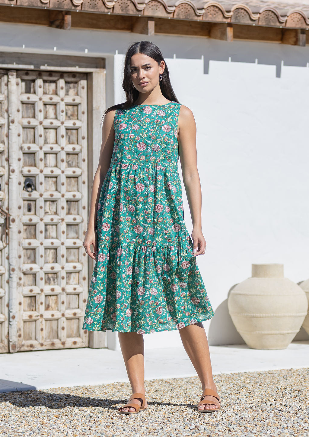 Woman wearing a green floral cotton midi dress standing in front of a textured wall and white door.