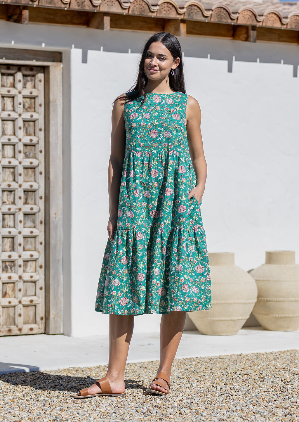 Woman wearing a green floral cotton midi dress standing in front of a white wall with wooden doors and vases.