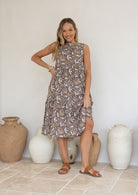 Woman wears a sleeveless, relaxed fit  floral cotton dress with tiered style, empire waist and pockets.