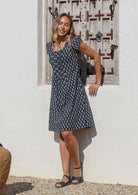 Woman posing in front of the white wall wears 100% cotton navy blue floral motif printed dress with cap sleeves and round neckline