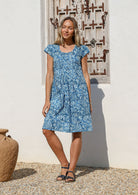 Woman wearing a blue floral cotton knee length dress with cap sleeves and a round neckline