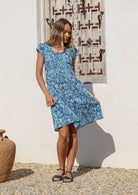 Woman swishing the skirt of her blue cotton floral knee length dress, paired with sandals