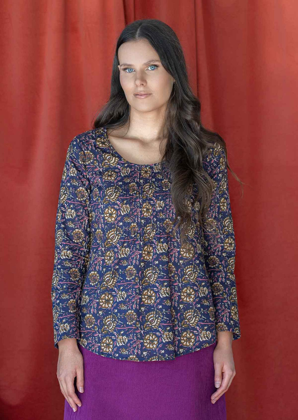 Woman wearing a 100% cotton long sleeved top in pink, cream and brown floral print on dark purple base.