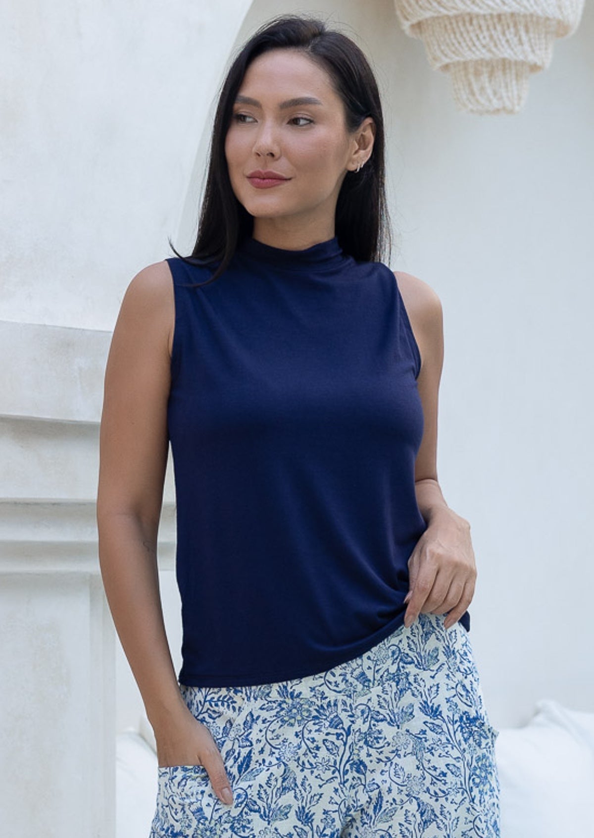 Woman wearing a navy sleeveless top with a mock turtle neckline and floral pants
