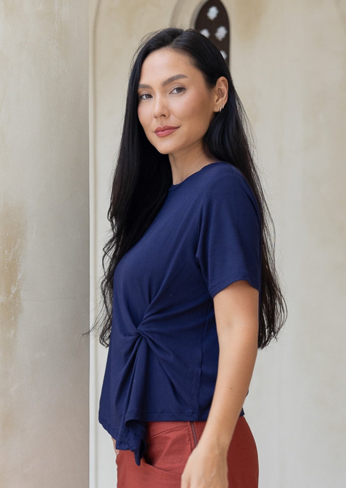 Woman wearing a blue top with a knot detail in the front, standing against a neutral wall.