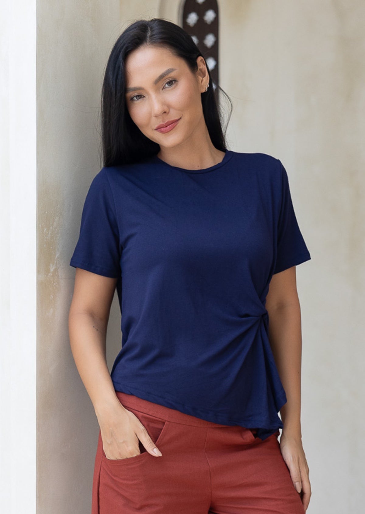 Woman wearing a navy blue short sleeve rayon top and rust pants with hand in pocket