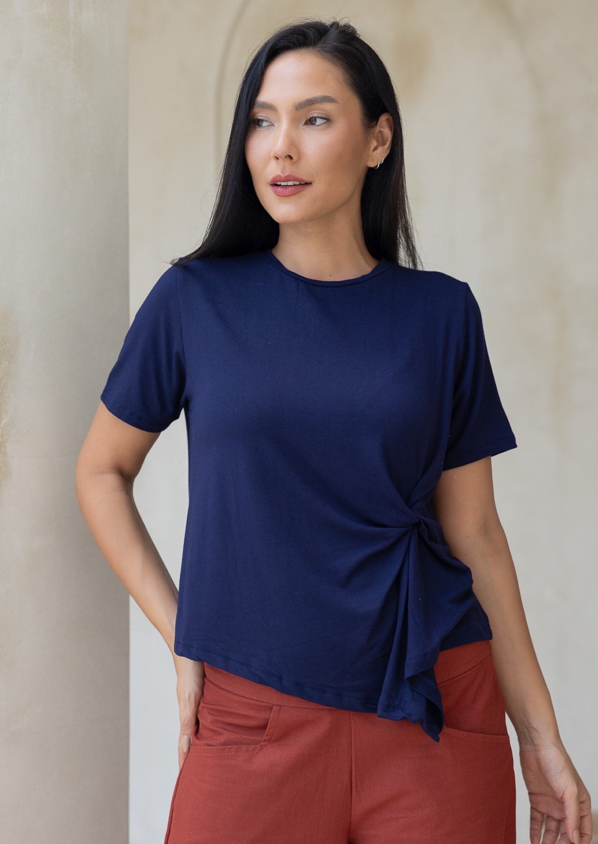 Woman wearing a navy blue short sleeved top with a knot detail, standing against a neutral background