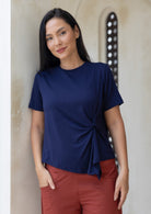 Woman wearing a navy blue top with a knot detail in the front, standing against a neutral wall.
