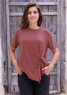 Woman wearing a terracotta short sleeve rayon top and black pants with hand in pockets