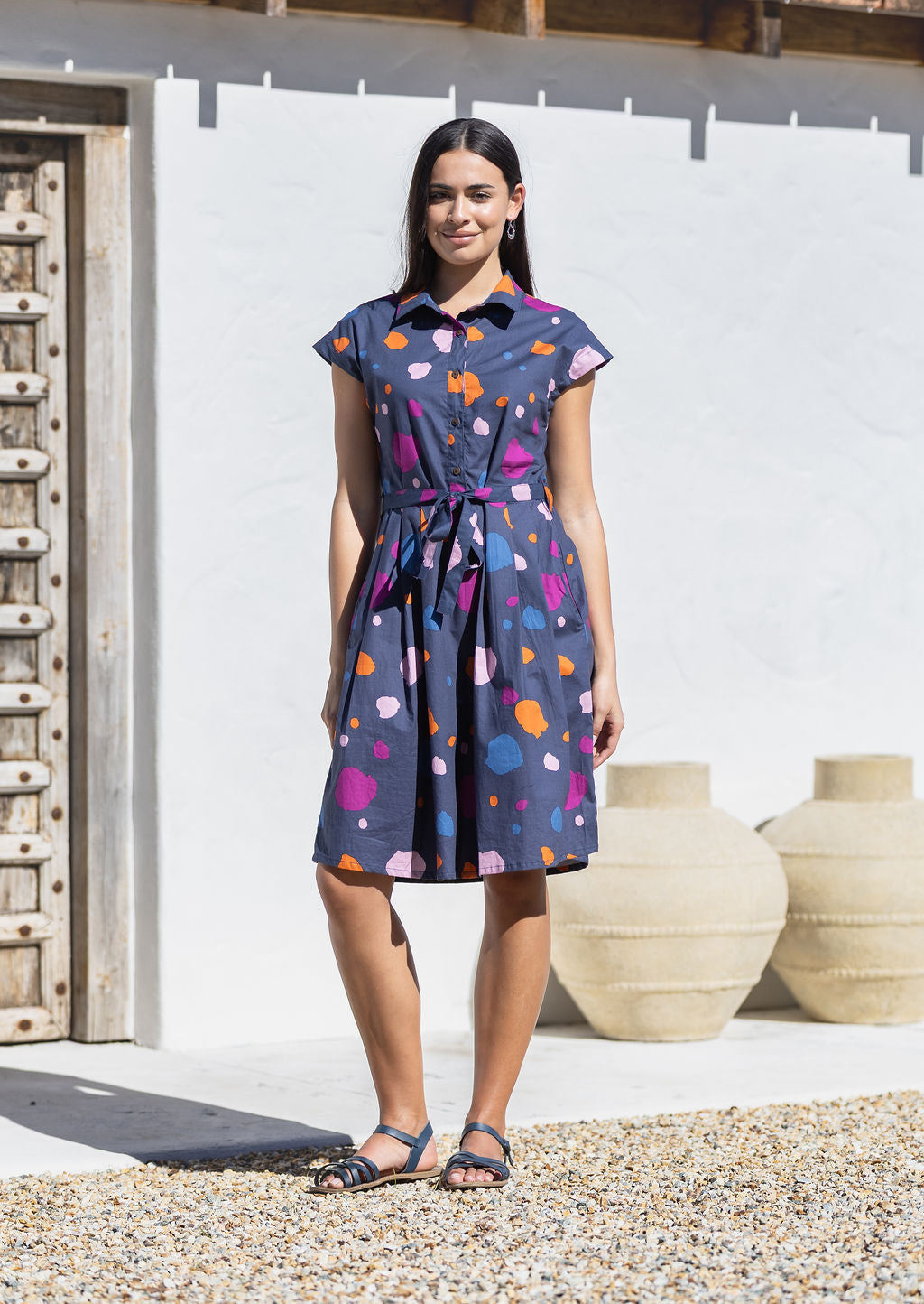 Woman wearing a cotton knee length day dress with a buttoned bodice, collar and cap sleeves