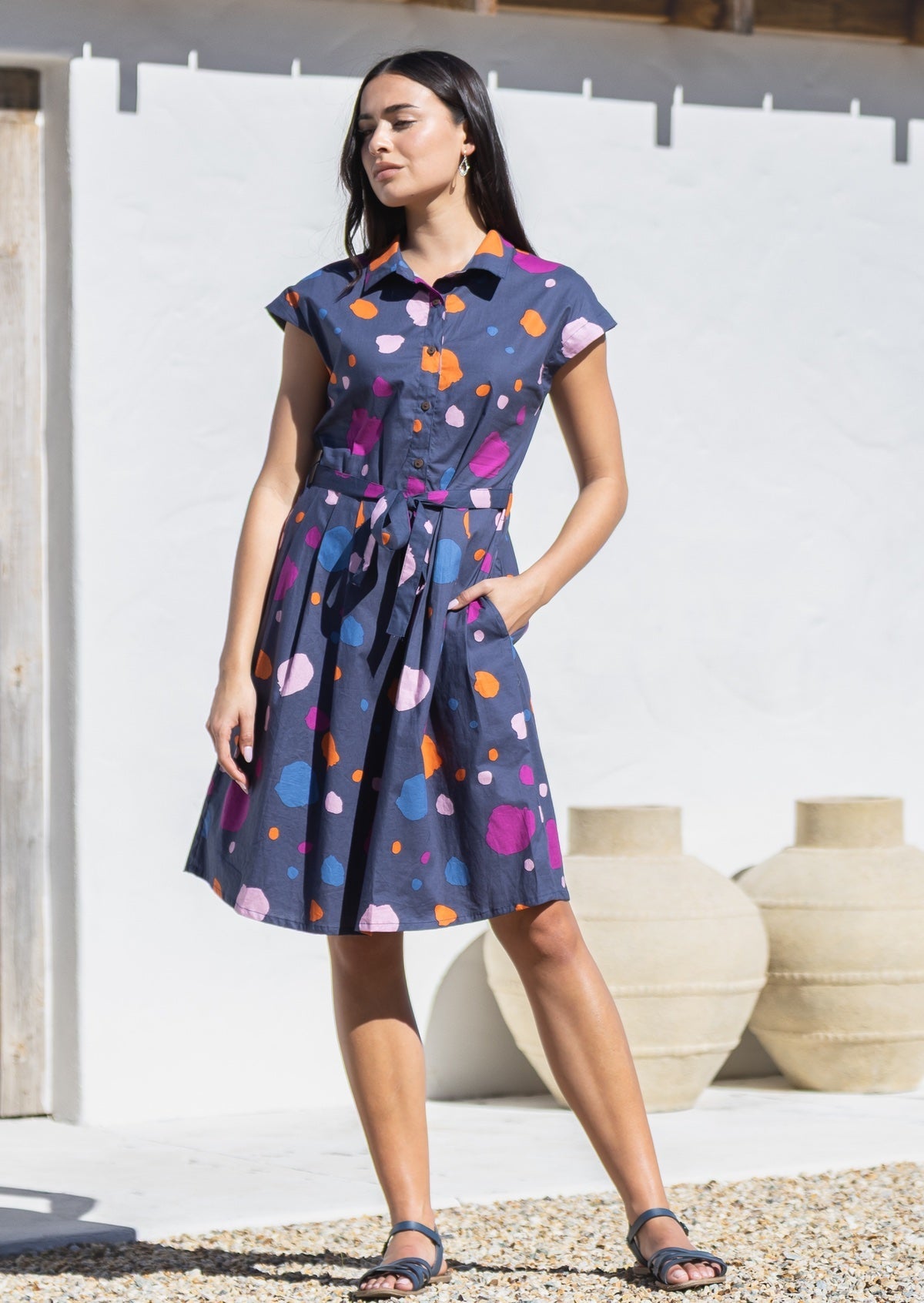 Woman wearing a knee length, colourful spot on blue base cotton dress with hand in pocket