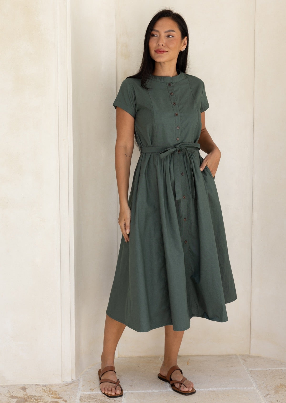 Woman wearing a moss green 50's style midi length dress with a hand in the hidden side pocket