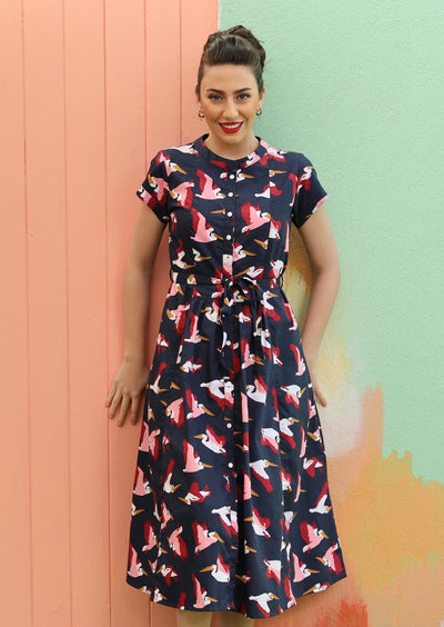 Model with dark hair wearing navy blue retro style dress with pelican print in pink and maroon