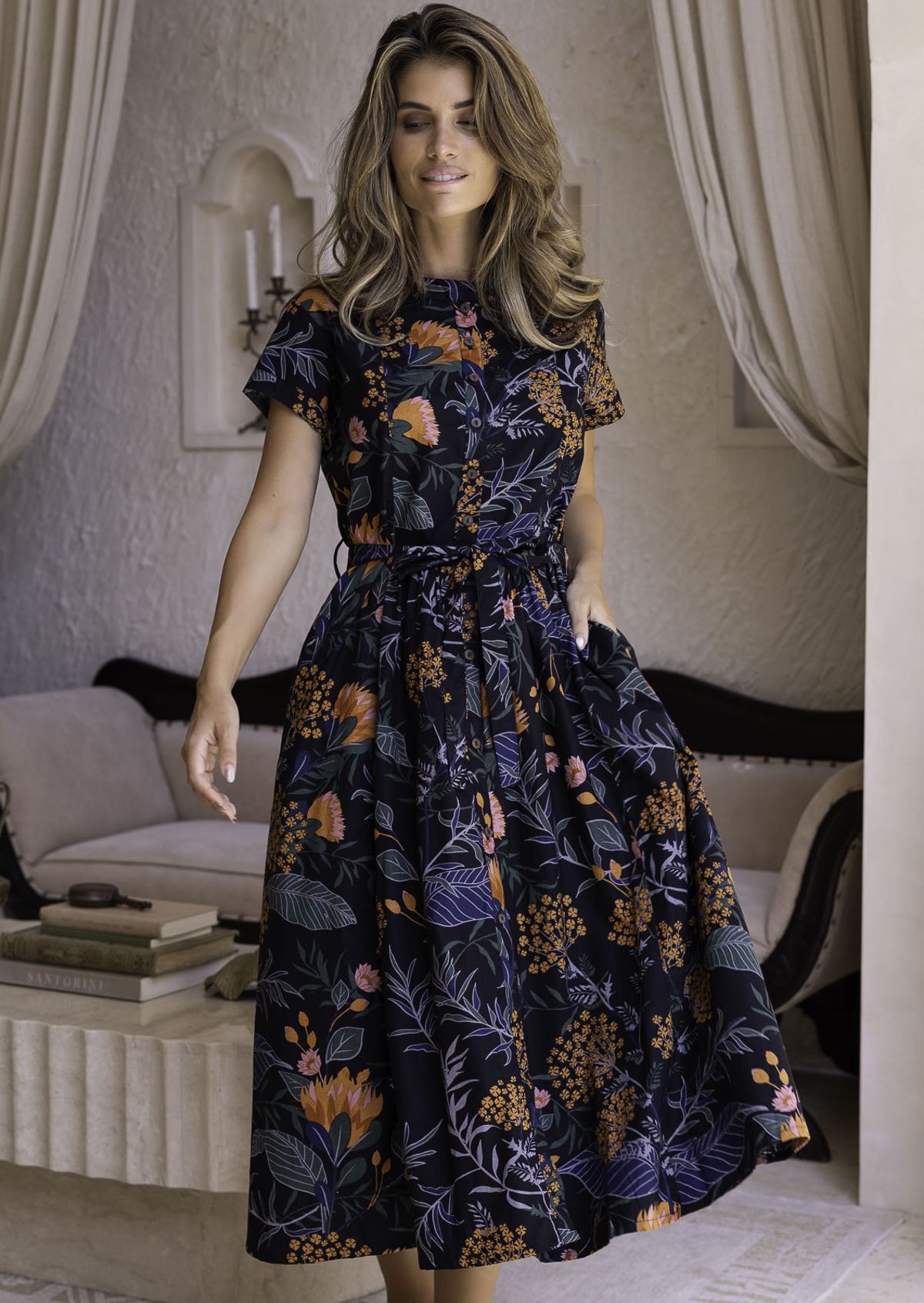Woman wearing a retro style dark floral dress with short sleeves, pockets and high round neckline.