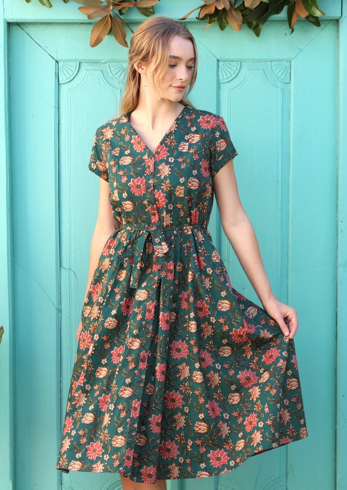 Model wears green cotton dress with folded V-neck, short sleeves and pockets.