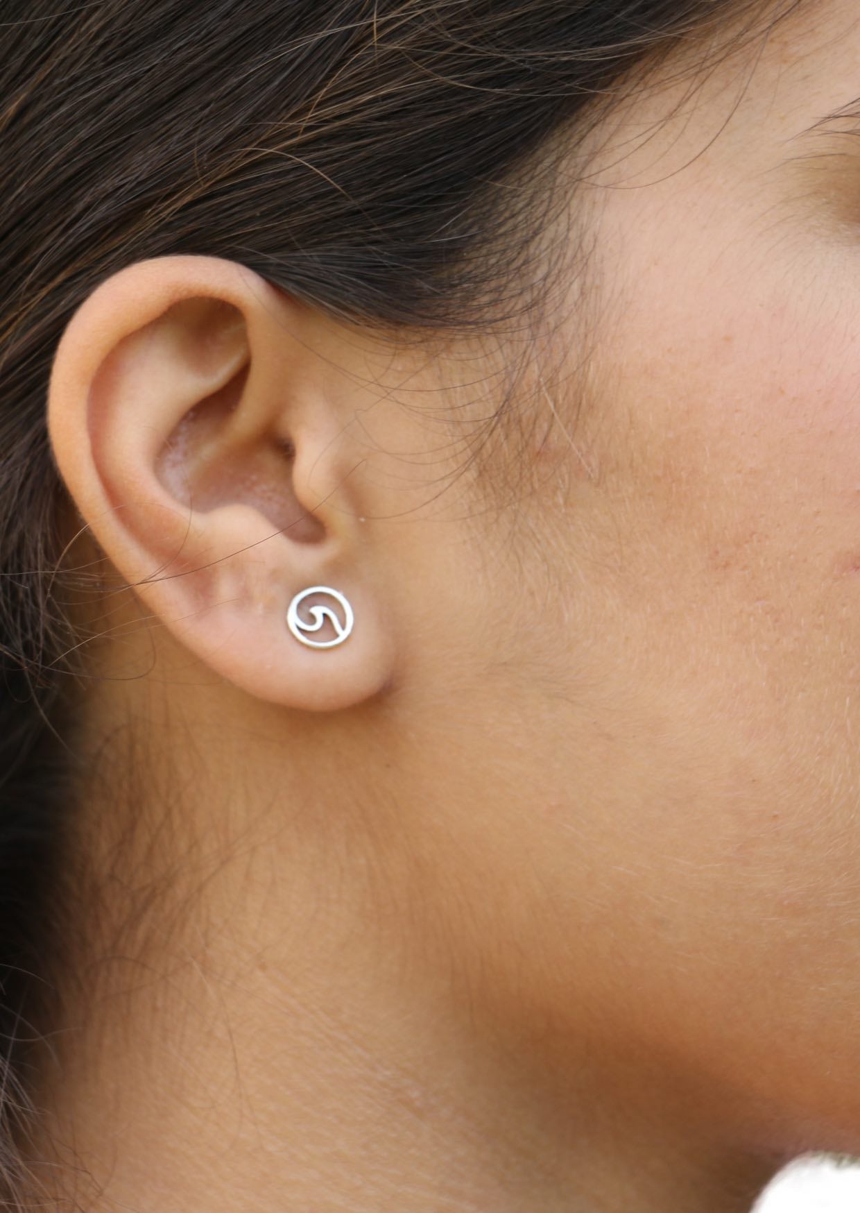 Close image of a person wearing a sterling silver circular studs with cutout wave design 
