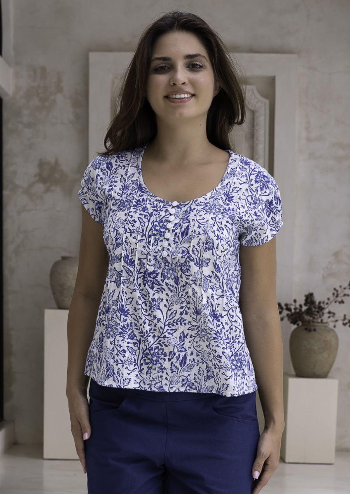 Woman wearing a white based blue floral print cotton top in an indoor setting.