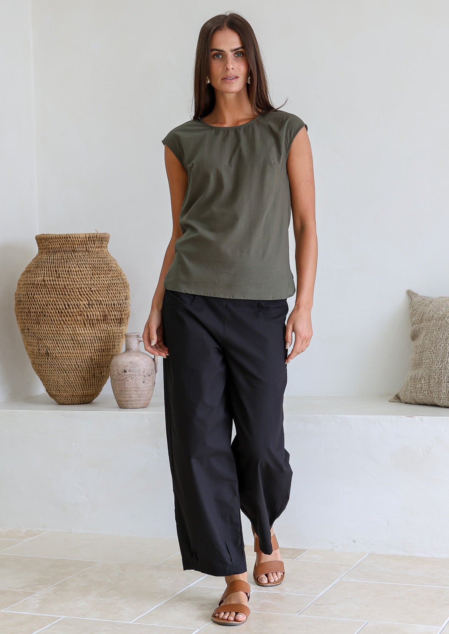 Woman wearing a muted green cotton top with bust darts and a round neckline, paired with black pants
