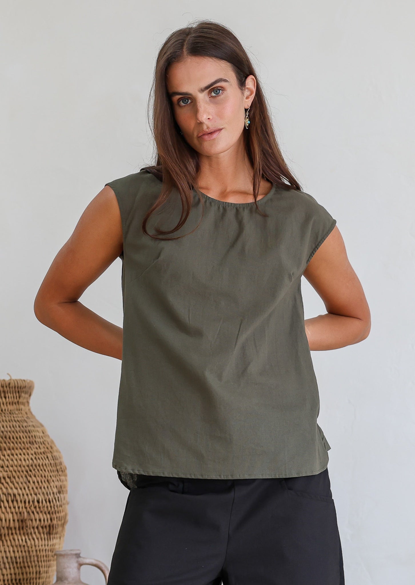Woman wearing a muted green sleeveless cotton sleeveless top with a round neckline
