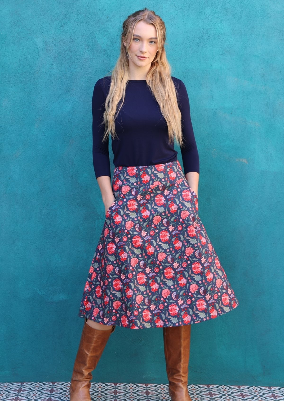 Model wears a beautiful navy blue skirt with red florals, pockets and a wide waistband.