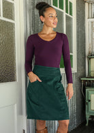 woman wearing a cotton corduroy skirt and basic top standing indoors with one hand in pocket