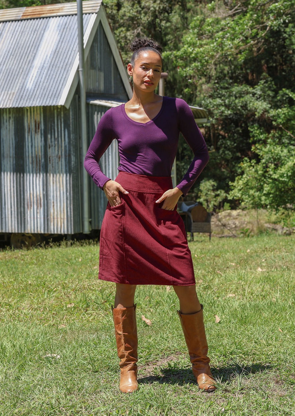 Woman wearing a basic top and cotton corduroy skirt in deep, luxurious, and intense red-purple hue with boots standing outdoors.