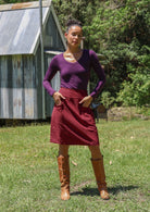 Woman wearing a basic top and cotton corduroy skirt in deep, luxurious, and intense red-purple hue with boots standing outdoors.