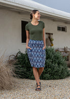 Woman standing with both hand in pockets wears navy based floral print cotton above knee length skirt piped detailing.