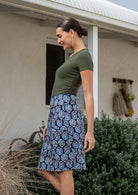 Woman posing sideways wears 100% cotton A-line skirt in navy based floral print, paired with olive green basic top.