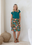 Woman stands in 100% cotton above knee length A-line skirt with piped detailing, pockets and a side zipper.