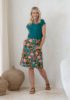 Woman wearing a basic top and floral  cotton skirt in olive green based with A-line shape, piped detailing and pockets.