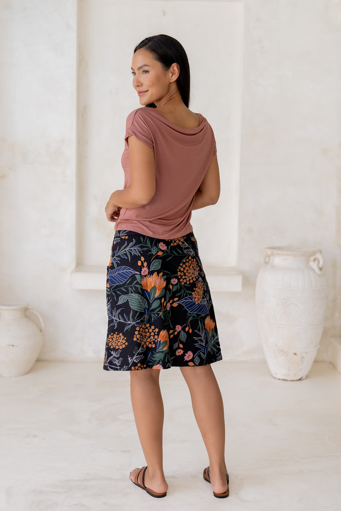 Model posing in a basic pink top and above knee length a-line cotton skirt in black based botanical print with side zipper and pockets