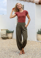 Woman in a terracotta basic top and green cotton pants with wide flat front waistband shirred at the back and cuffed ankles