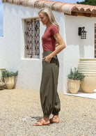 Woman standing with hands in pockets wearing a 100% cotton relaxed fit olive green pants with shirred back waist and cuffed ankles