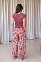 Woman stands backwards wearing floral cotton wide leg pants with buttoned ankle paired with pink basic top