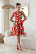 Woman wearing retro inspired cotton knee length dress in vibrant red backdrop featuring elegant multicoloured floral vines.