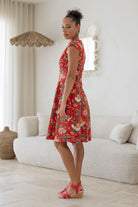 Model posing sideways in a beautiful cotton dress with red backdrop featuring elegant multicoloured floral vines.