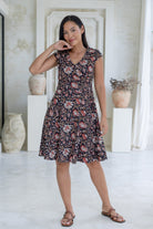 Model wears knee length, retro style black floral cotton dress with crossover bodice, cap sleeves and pockets.