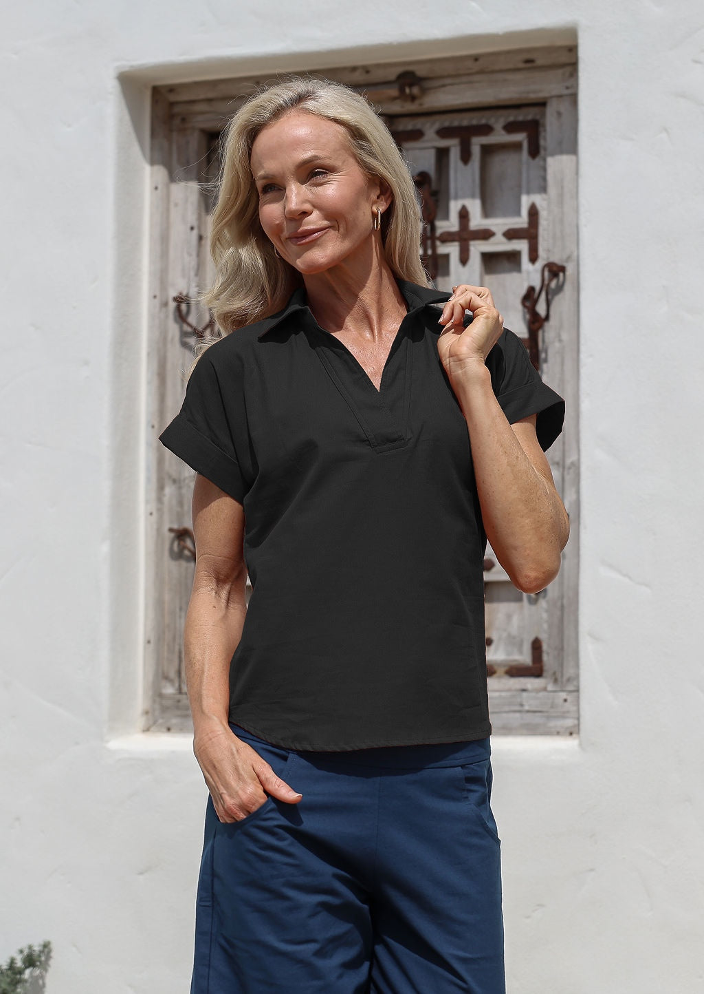 Woman wearing a black cotton relaxed fit top with short sleeves and a collar, paired with blue pants